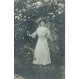1910 - Young woman in front of a rose bush. In elegant dress, full-length photo. Original paper image. Postcard, photo sheet. (2791914)