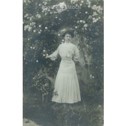   1910 - Young woman in front of a rose bush. In elegant dress, full-length photo. Original paper image. Postcard, photo sheet. (2791914)